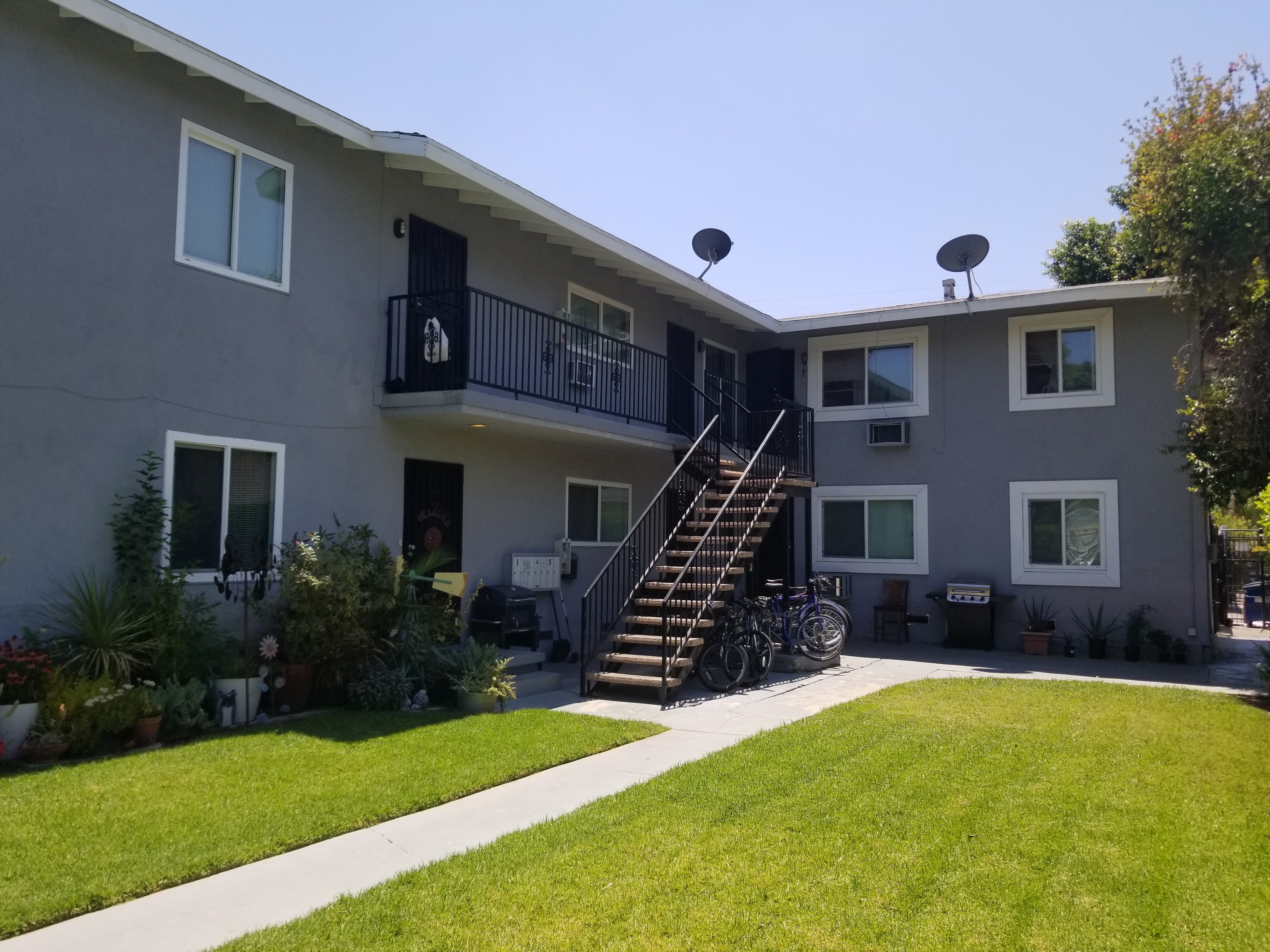 A grey two-story apartment building with a balcony and stairs leading to the second floor.